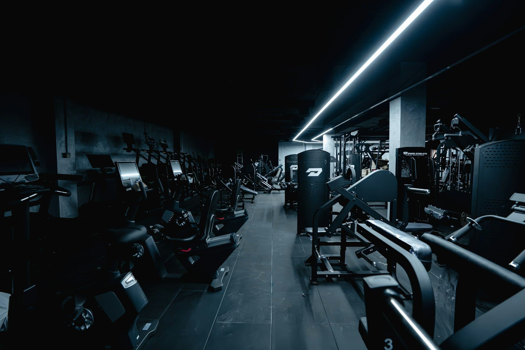Gimnasio comercial con iluminación lineal, máquinas de fuerza y cardio