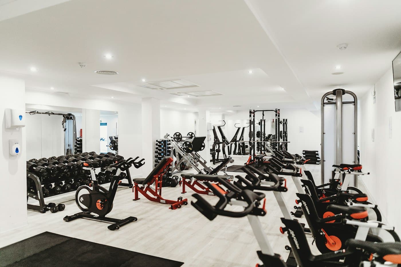 Gimnasio comercial con máquinas rojas, bicicletas y zona de peso libre